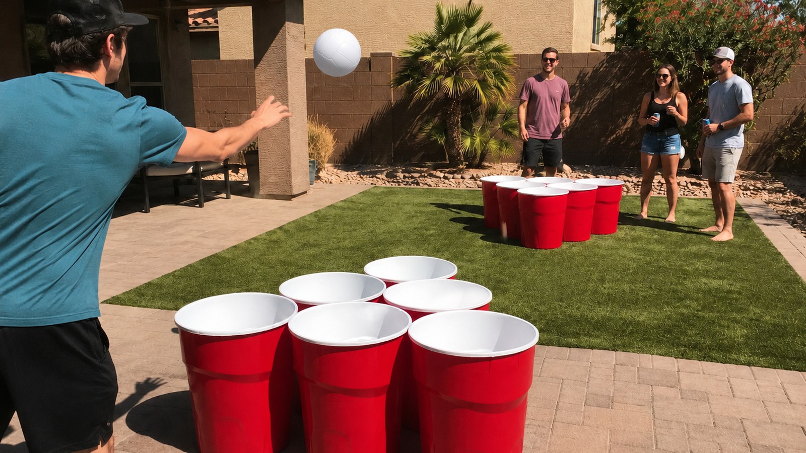 Giant yard pong rental game with two opposing sets of six red cups and a white volleyball in a Mesa backyard